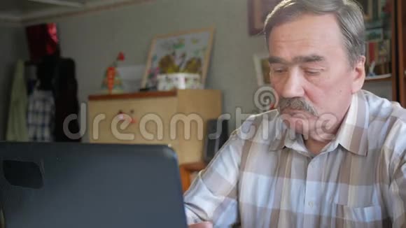一个有胡子的老人坐在笔记本电脑后面解决问题他认真地看着班长视频的预览图