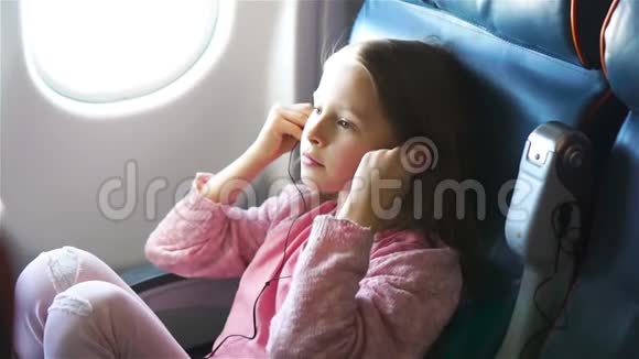 可爱的小女孩乘飞机旅行可爱的孩子在飞机窗户附近听音乐视频的预览图