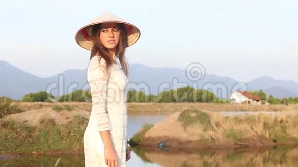 穿着越南服装和帽子的金发女孩在池塘边摆姿势视频的预览图