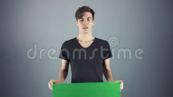 年轻男子身穿黑色衬衫手持绿色钥匙片海报灰色背景视频的预览图