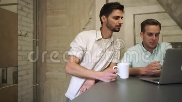 两个喝咖啡的年轻职业男士看着电脑和聊天视频的预览图
