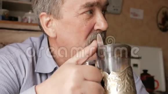 有胡子的老人端着一杯热饮和饮料他坐在窗边在家吃早饭视频的预览图