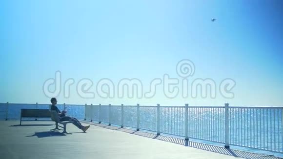 一个人坐在长凳上在海上发射一架无人机视频的预览图