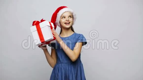 圣诞老人帽子摇礼品盒里快乐的微笑女孩视频的预览图