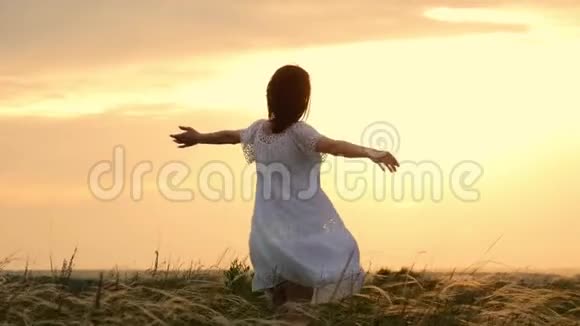 美丽的女孩穿着白色的裙子在夕阳下穿过美丽的田野年轻女子在草地上慢跑视频的预览图