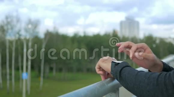 现代年轻人带智能手表的户外肖像在绿树和美丽的蓝天的背景下视频的预览图