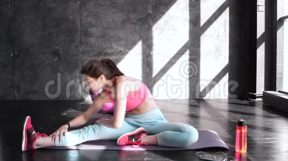 致力于健身前景是一位穿着运动服装坐在地板上做伸展运动的年轻美女视频的预览图