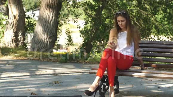 一位美丽的年轻女子坐在公园长椅上自拍视频的预览图