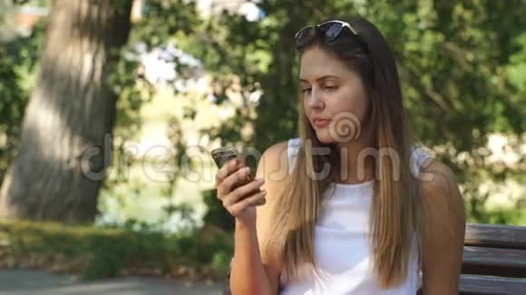 公园长椅上的年轻女人用你的电话视频的预览图