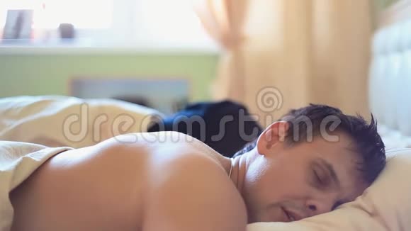 清晨女人醒来在床上和熟睡的强壮丈夫交谈视频的预览图