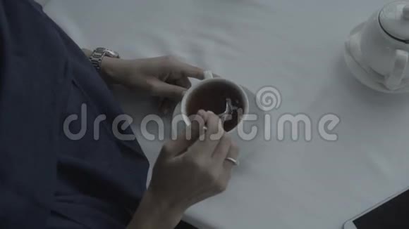一个穿着蓝色裙子的女人用勺子在白色桌子上搅拌咖啡视频的预览图