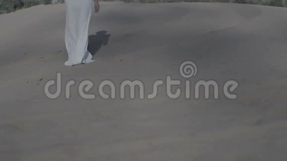 穿着白色连衣裙在海滩沙丘上行走的女性双脚太阳落山影子慢动作前视平色视频的预览图