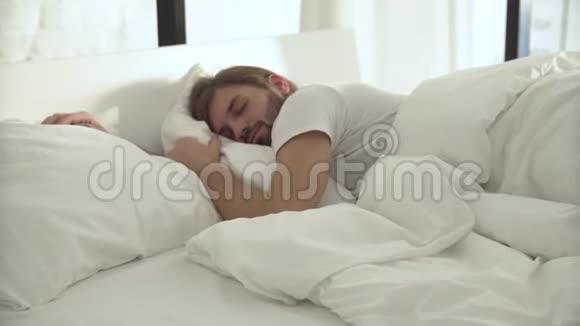 在床上躺着的睡客带着白色的亚麻布在轻卧室视频的预览图