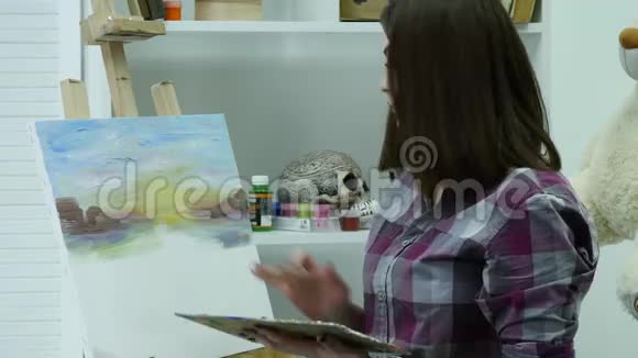 艺术家在画布上画一个女人并涂上一层宽的画笔帆布站在画架上画家在画架上画画视频的预览图