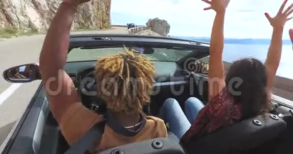 乘坐红色敞篷车在沿海公路上挥舞手臂的朋友的后景视频的预览图