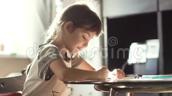 小女孩在家里用铅笔画画坐在桌子旁在朝阳下的孩子视频的预览图