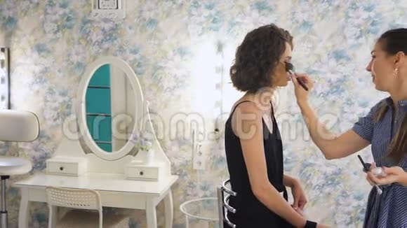 年轻的女化妆师在明亮的工作室工作在客户身上化妆视频的预览图