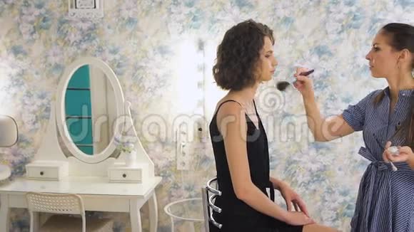 年轻的女化妆师在明亮的工作室工作在客户身上化妆视频的预览图