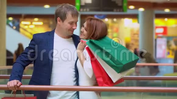 年轻夫妇在购物中心谈论和享受购物套餐带着多色包装的情侣微笑视频的预览图