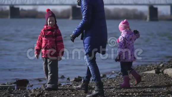 一位年轻的母亲和两个小女儿正走在河的城堤上慢动作视频的预览图