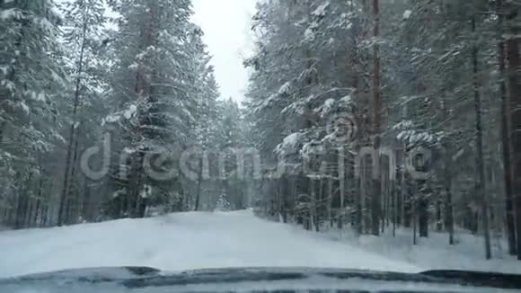 一辆汽车在降雪中沿着一条下雪的森林道路行驶视频的预览图