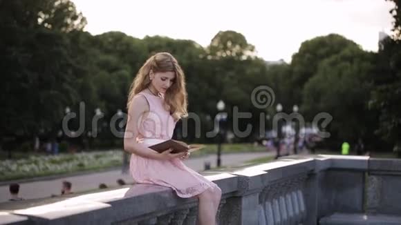 年轻有魅力的女孩读一本书对夏天的公园感兴趣视频的预览图