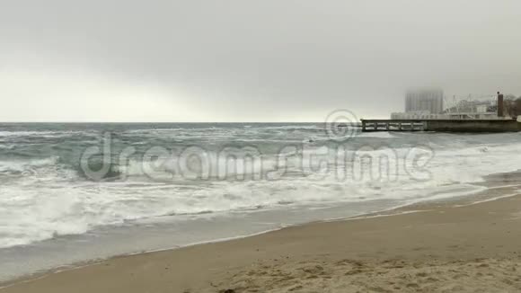 沙滩和波涛汹涌的大海码头和高楼大厦在雾中乌云密布视频的预览图