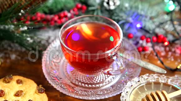 冬茶一杯带蜂蜜牛角面包或饼干的茶雪中圣诞树的一根树枝圣诞灯视频的预览图