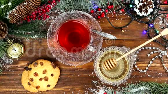 冬茶一杯带蜂蜜牛角面包或饼干的茶雪中圣诞树的一根树枝圣诞灯视频的预览图