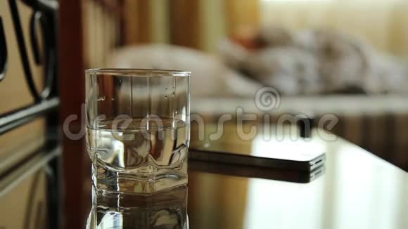 特写一杯水和一个电话年轻的女人醒来伸展手臂在床上在早上模糊的焦点视频的预览图