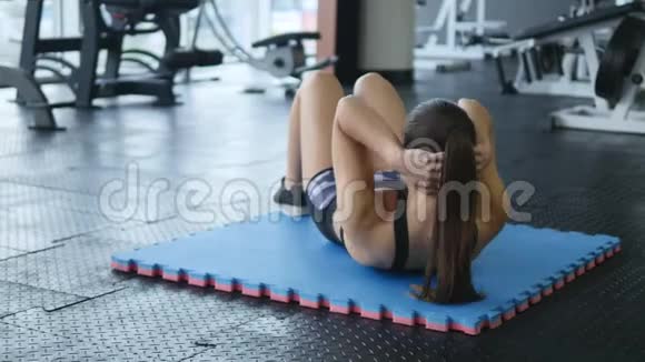 年轻女子在健身房的地板上将压力的斜肌肉泵入视频的预览图