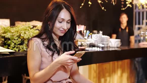 坐在酒吧里浏览智能手机的年轻漂亮女孩视频的预览图