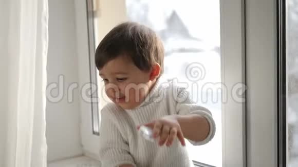 冬天穿白色针织毛衣的男孩坐在窗边视频的预览图