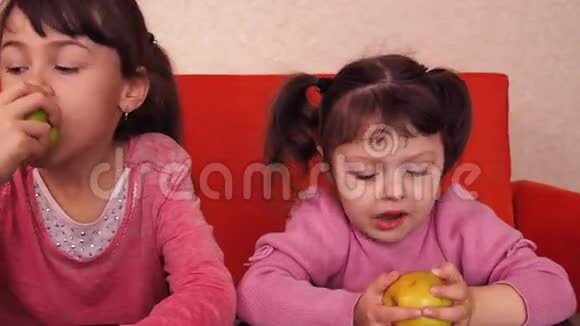 孩子们吃苹果两个姐妹坐在橙色的沙发上吃黄色的苹果视频的预览图
