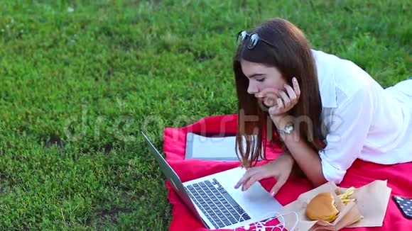 年轻的女性按下键盘在绿草上吃快餐视频的预览图