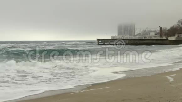 沙滩和波涛汹涌的大海码头和高楼大厦在雾中乌云密布视频的预览图