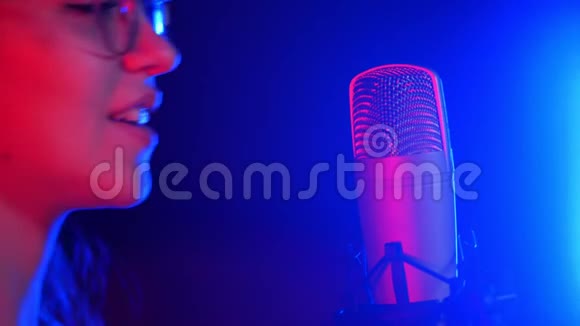 一个戴着耳机在录音室唱歌的年轻情绪化的女人霓虹灯照明视频的预览图