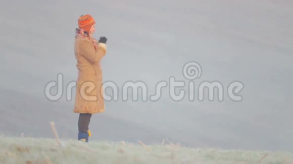 在田野里穿暖和衣服的年轻女人日出时在场的年轻女子视频的预览图