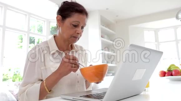 印度高级妇女在吃早餐时使用笔记本电脑视频的预览图