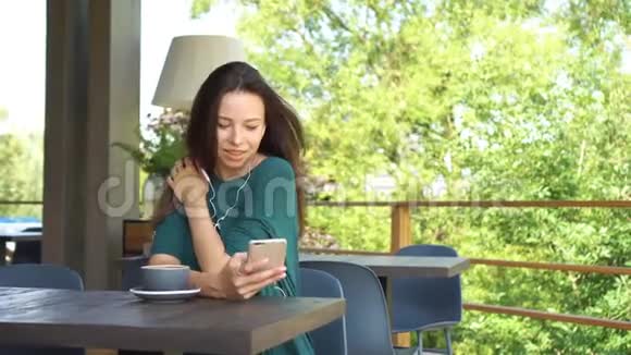 女人在智能手机上使用应用程序在咖啡馆里喝咖啡微笑着在手机上发短信美丽的年轻女性视频的预览图