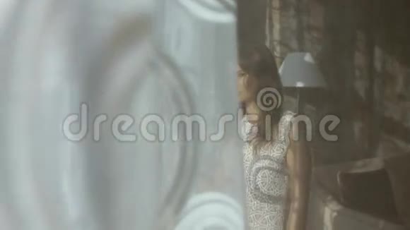 漂亮的年轻女子站在酒店房间的窗户前摆姿势视频的预览图