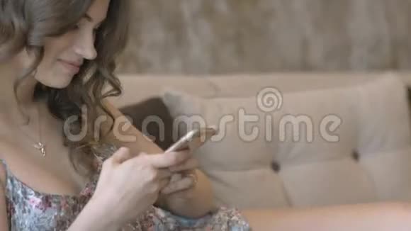 穿着睡衣的迷人女孩拿着手机坐在沙发上视频的预览图