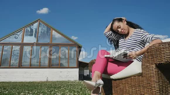 漂亮的小女孩坐在柳条扶手椅上在大自然看书视频的预览图