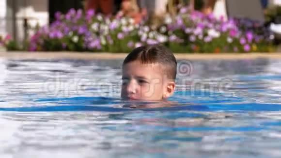 快乐的男孩在酒店的一个有蓝色水的游泳池里游泳慢动作视频的预览图