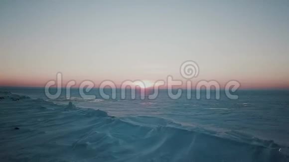 日落于冬湖高空拍摄冬季冰雪覆盖的大型松林环绕的冰湖鸟瞰图视频的预览图