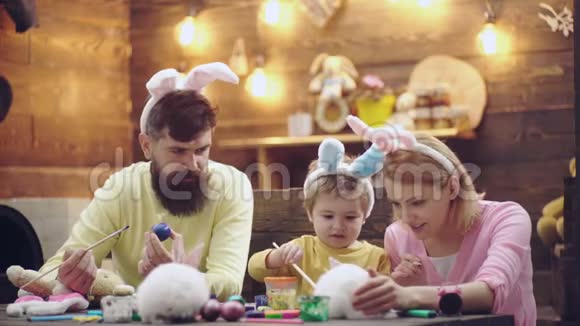 母亲父亲和儿子正在画鸡蛋幸福的家庭正在为复活节做准备可爱的小男孩穿着兔子视频的预览图