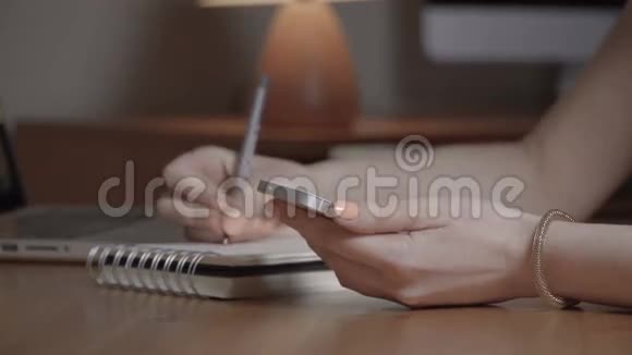 女性手拿着白色的手机在笔记本上写一些东西视频的预览图