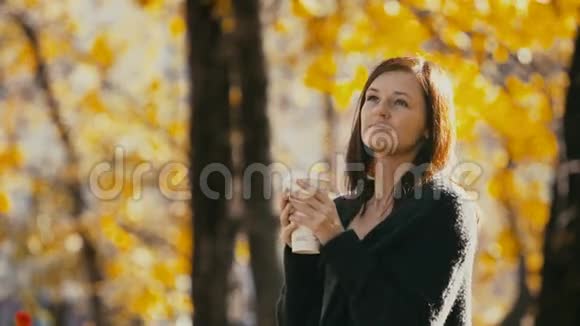 在秋天公园喝热咖啡的年轻女子视频的预览图