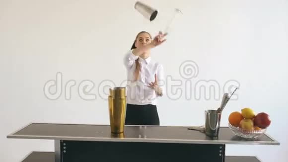 专业调酒师女孩在白色背景工作室的移动酒吧桌上摆弄瓶子和摇动鸡尾酒视频的预览图