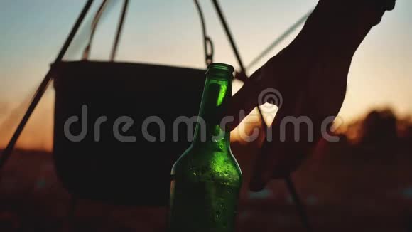 点燃一个大锅篝火一瓶啤酒在日落剪影露营特写旅游户外生活方式休闲旅游视频的预览图